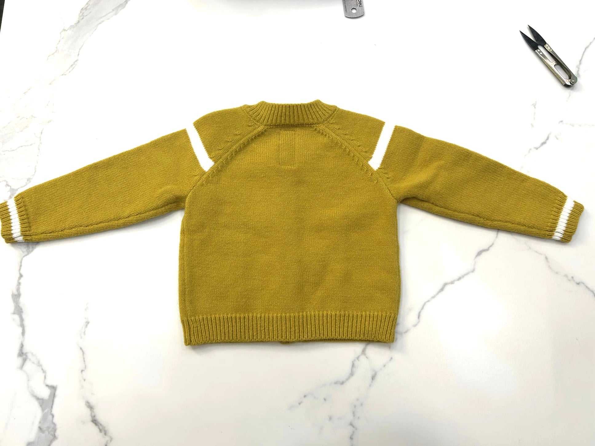 Yellow sweater with white stripes on sleeves on a marble surface