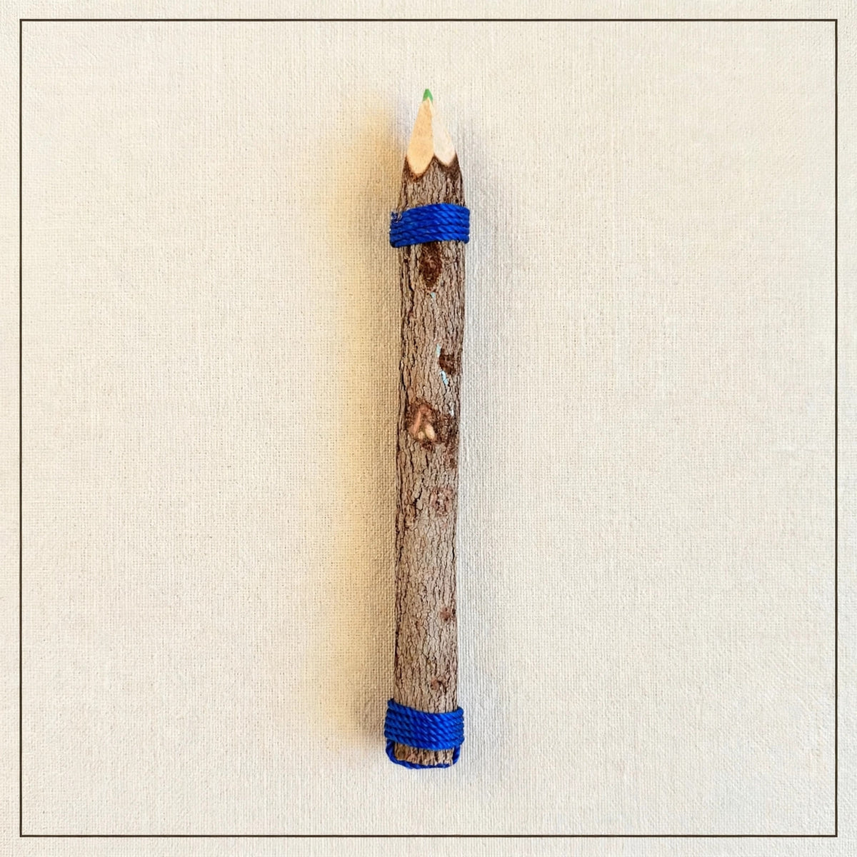 Back of a big hand-carved wooden coloring pencil showing natural tree bark with blue twine