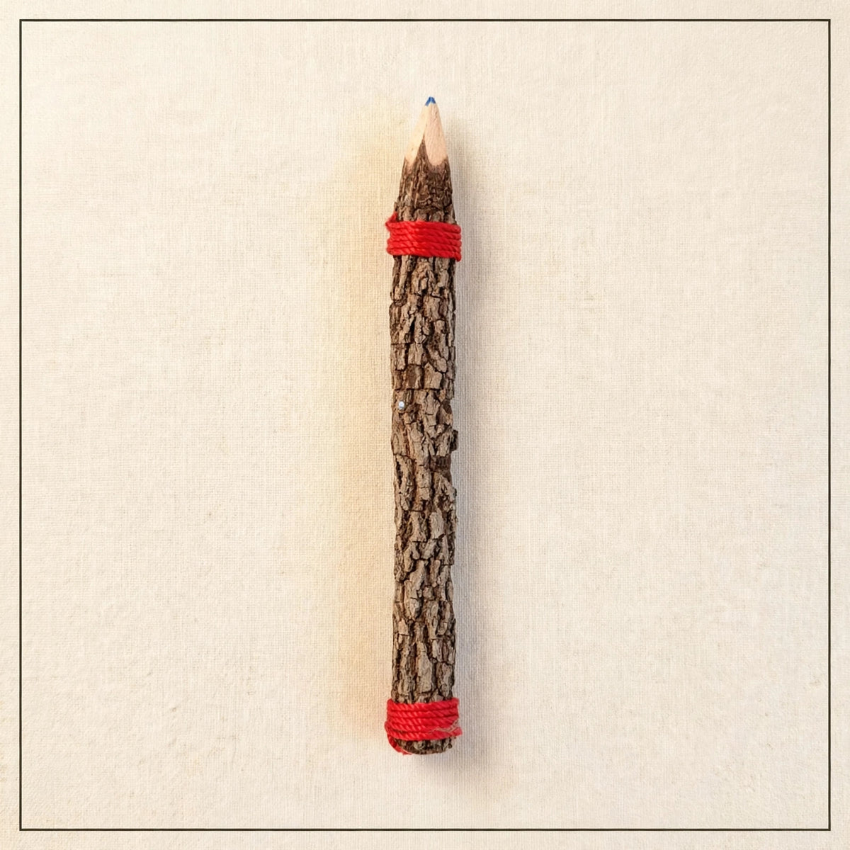 Back of a big hand-carved wooden coloring pencil showing natural tree bark with red twine