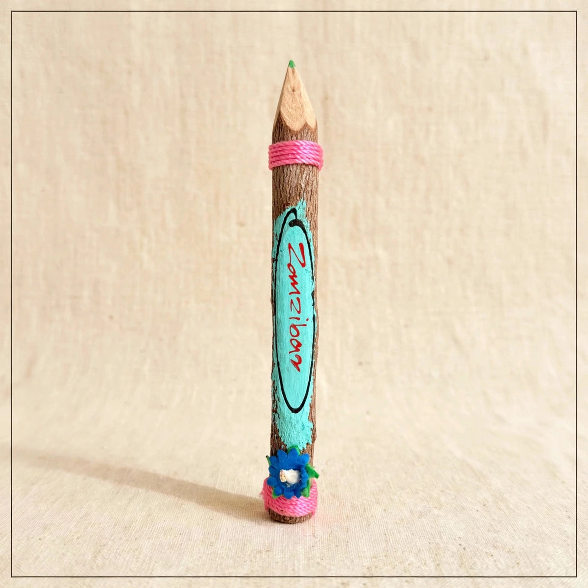 Big turquoise hand-carved wooden coloring pencil with pink twine and the hand-painted word Zanzibar, green tip