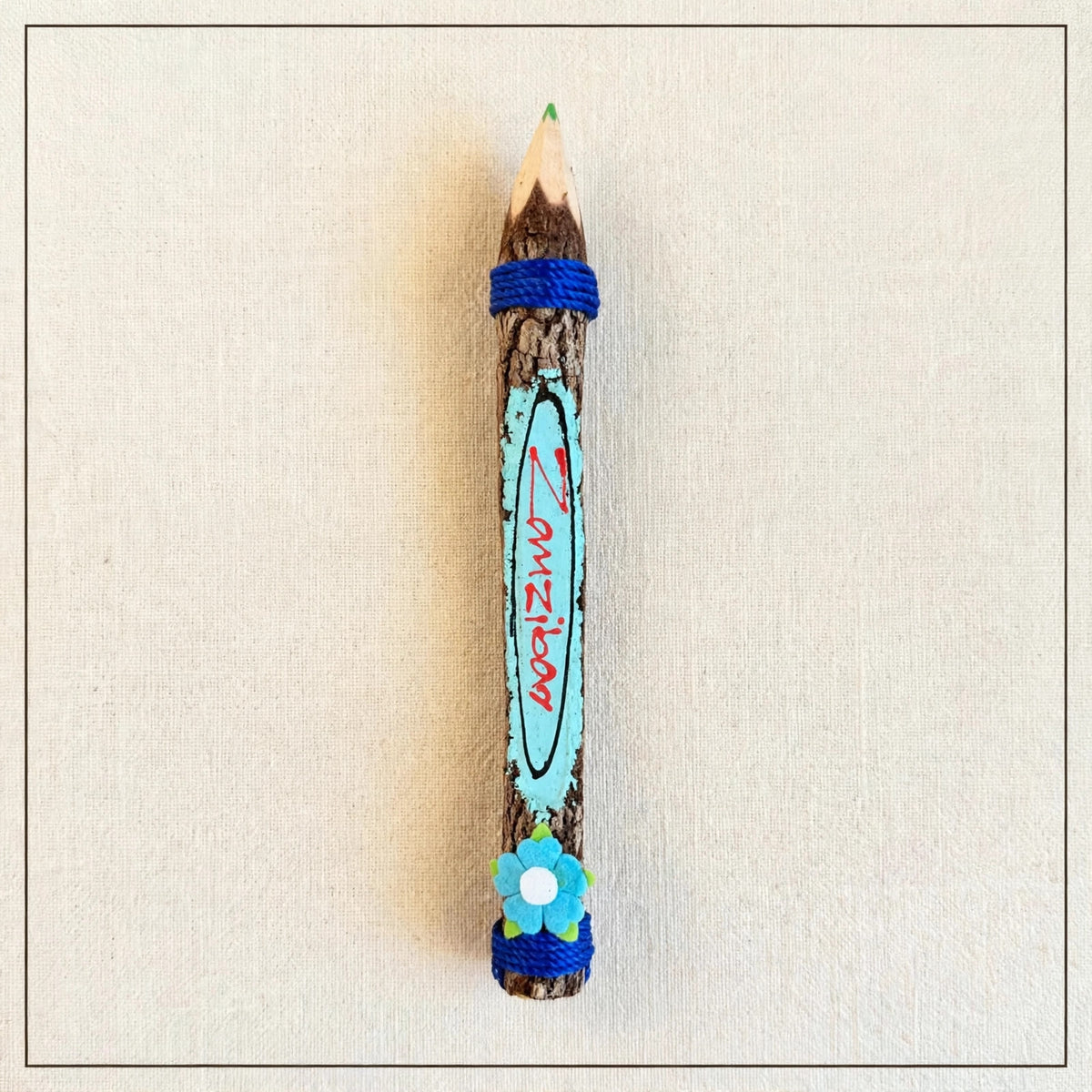 Big turquoise hand-carved wooden coloring pencil with blue twine, a blue felt flower and the hand-painted word Zanzibar