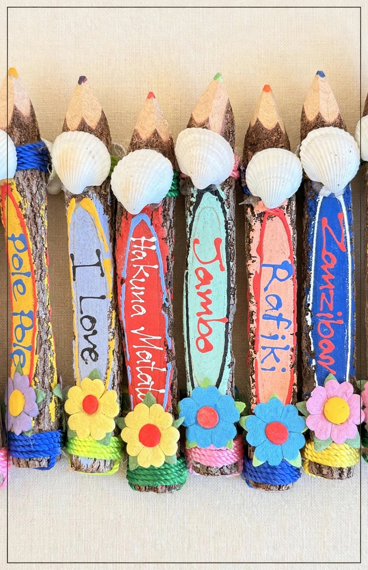Close-up of hand-carved wooden coloring pencils on cream linen with real seashells and Swahili words — Hakuna Matata, Jambo, Rafiki