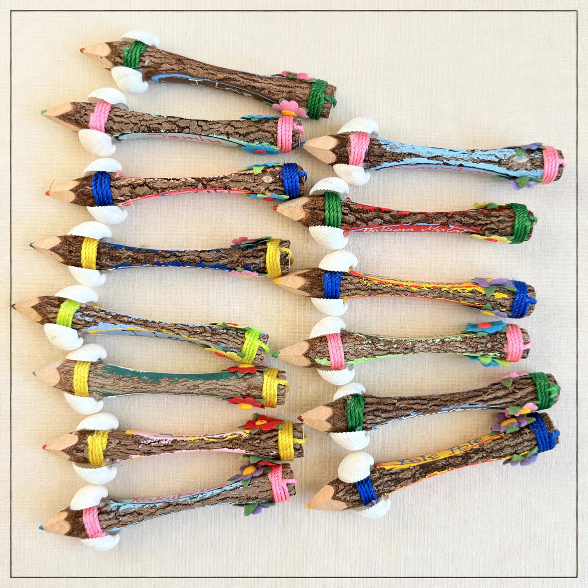 Small hand-carved wooden coloring pencils lying flat on cream linen showing natural bark backs and real seashells