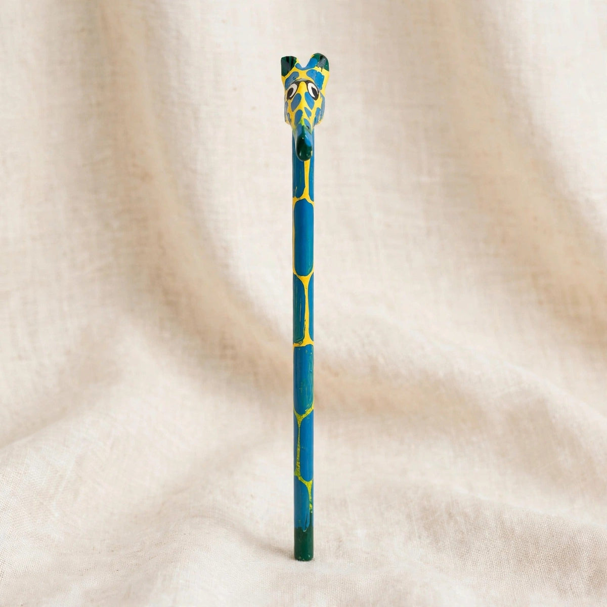 Front view of a hand-carved wooden pencil with a yellow giraffe head with blue spots