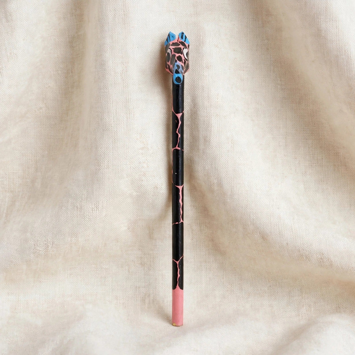 Front view of a hand-carved wooden pencil with a pink giraffe head with black spots
