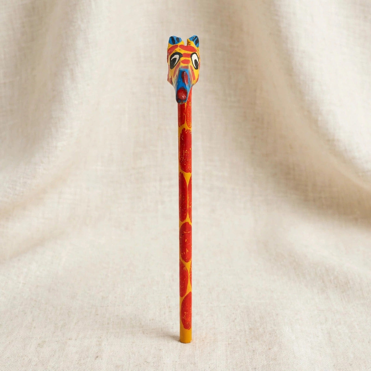 Front view of a hand-carved wooden pencil with a yellow giraffe head with red spots