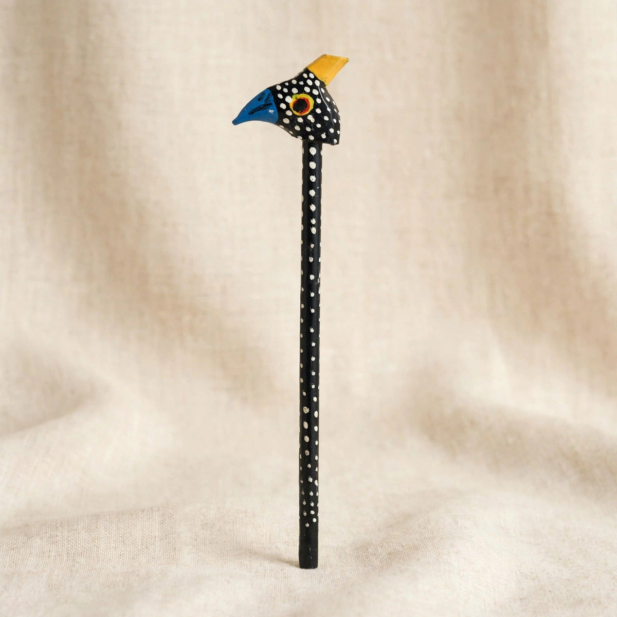 Hand-carved wooden pencil with a guinea fowl head, black with white dots, a blue beak and a yellow crest