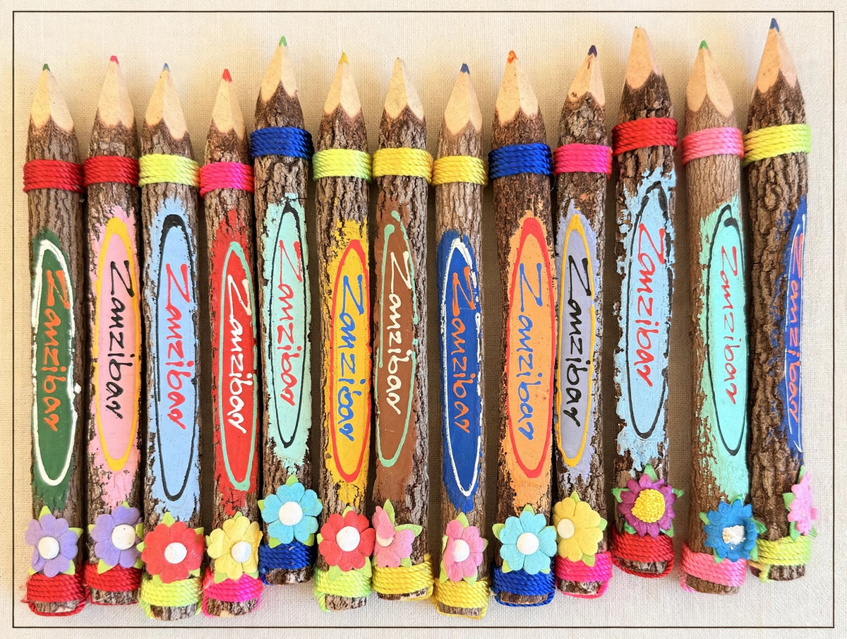 Row of big hand-carved wooden coloring pencils from Zanzibar on cream linen, natural bark with hand-painted designs