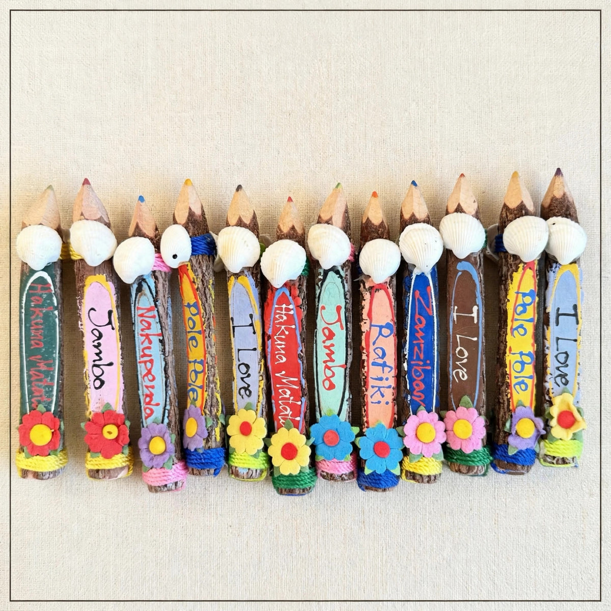 Row of small hand-carved wooden coloring pencils from Zanzibar on cream linen with real seashells and felt flowers