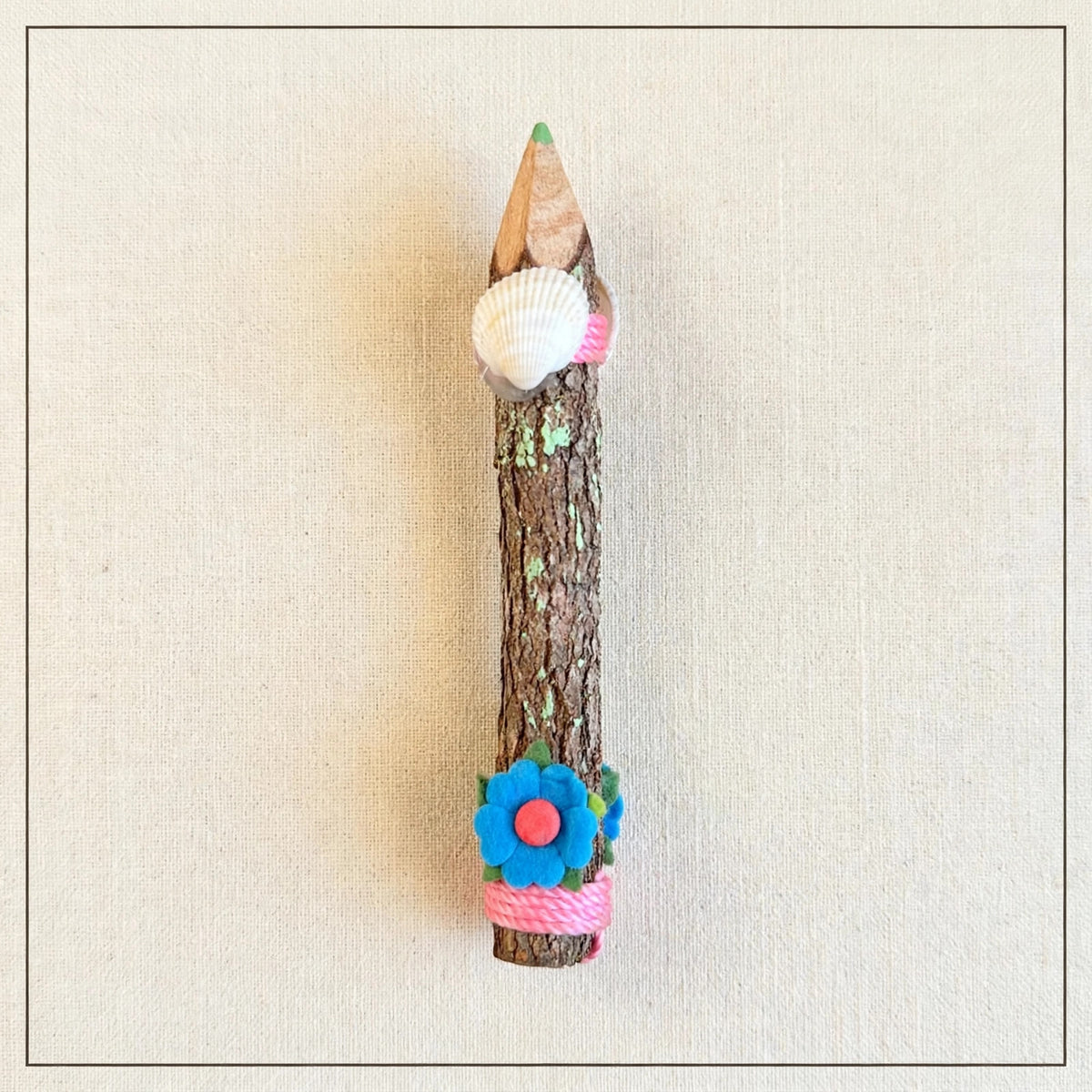 Back of a small hand-carved wooden coloring pencil showing natural bark and a real seashell