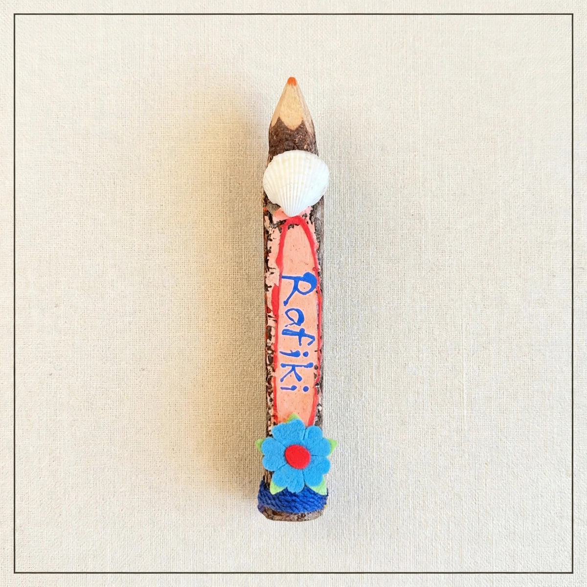 Orange small hand-carved wooden coloring pencil with a real seashell and the hand-painted word Rafiki